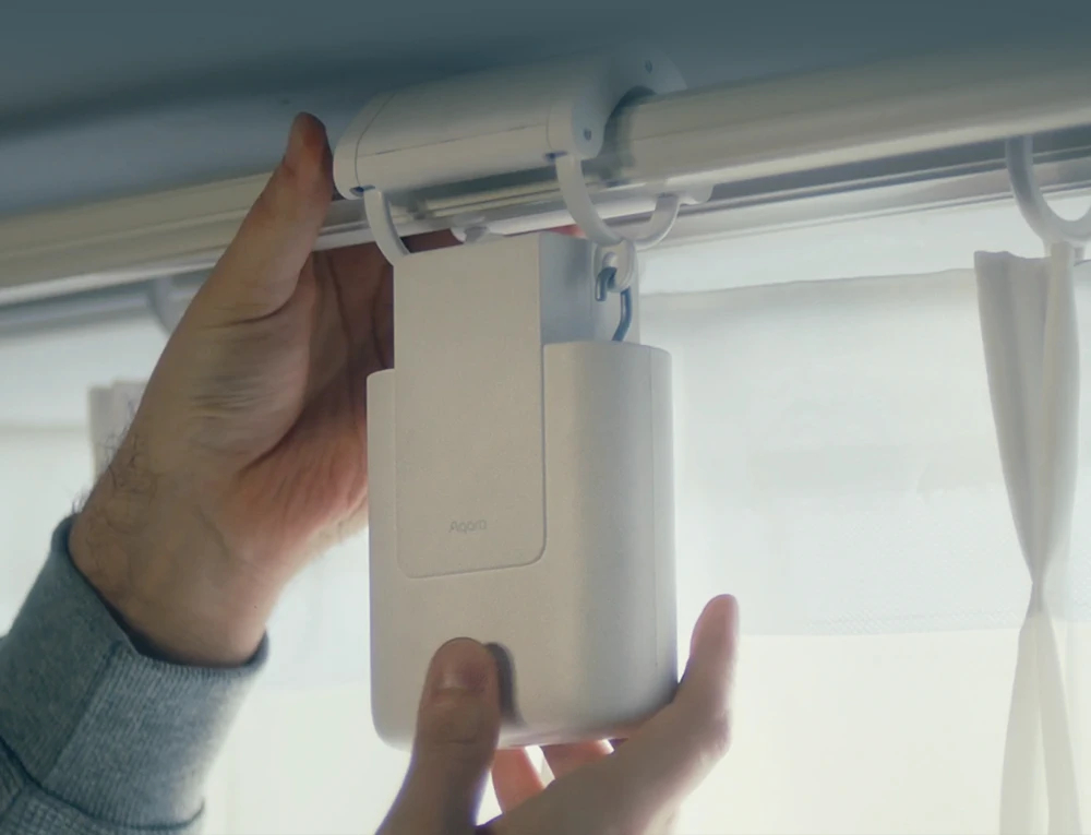 Ręce instalujące białe urządzenie smart home na szynie zasłony.