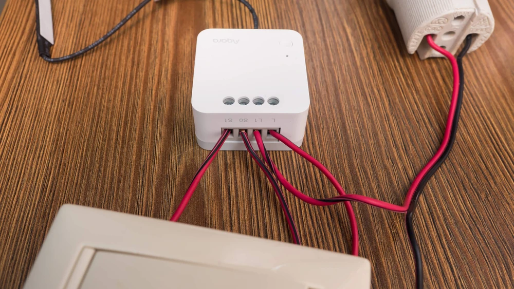 Biały inteligentny przełącznik z przewodami podłączonymi do gniazda ściennego i oprawy oświetleniowej.