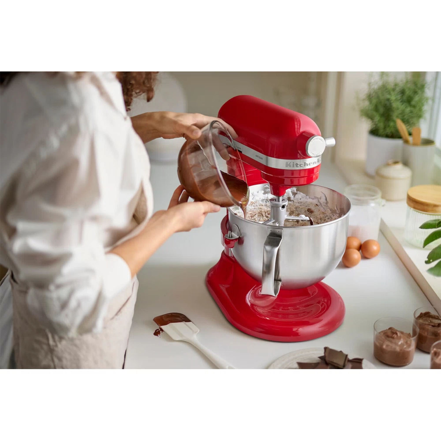 Un mixer KitchenAid rosso con una donna che versa ingredienti nella ciotola.