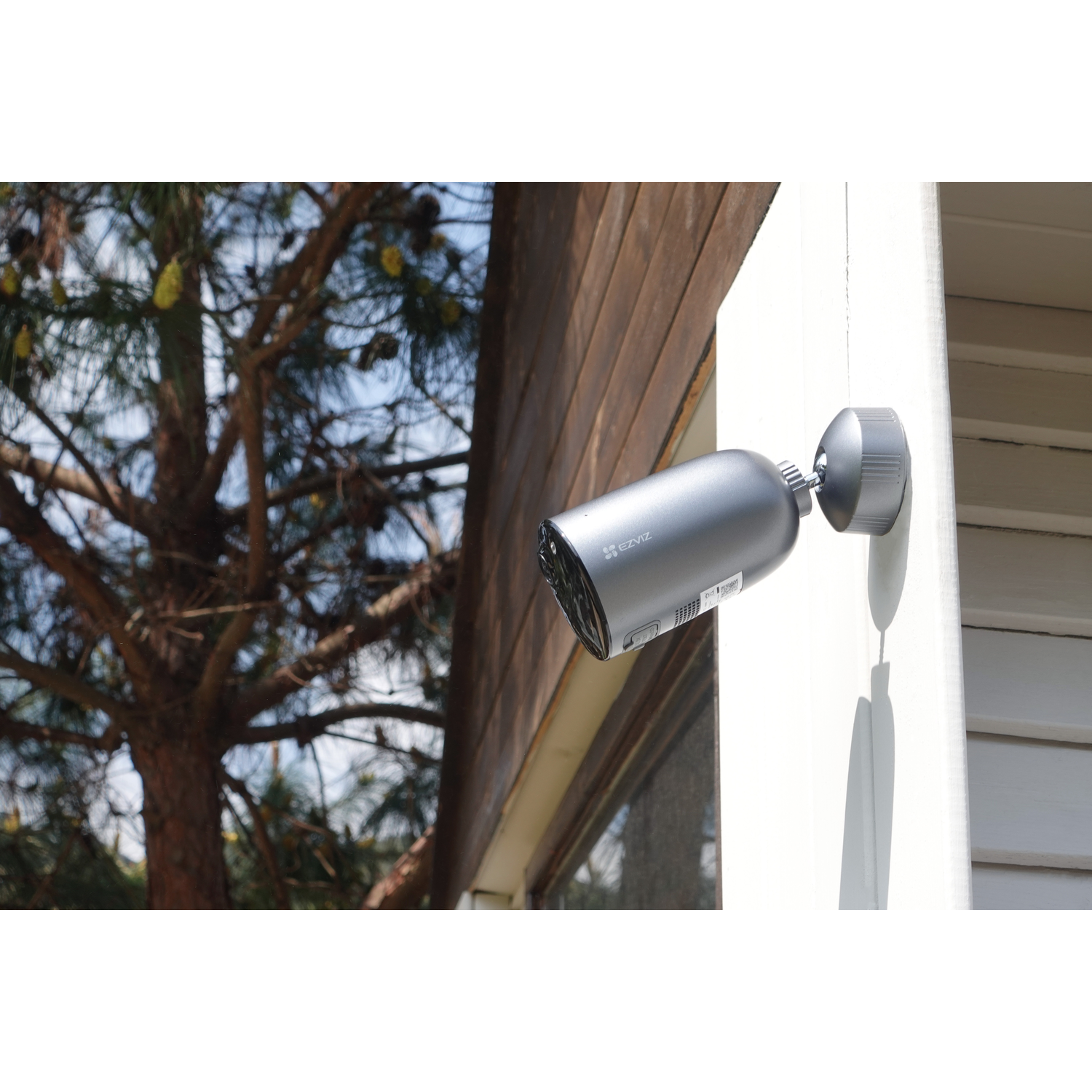 Silver security camera mounted on a white wall. Features a lens and a pivoting base.