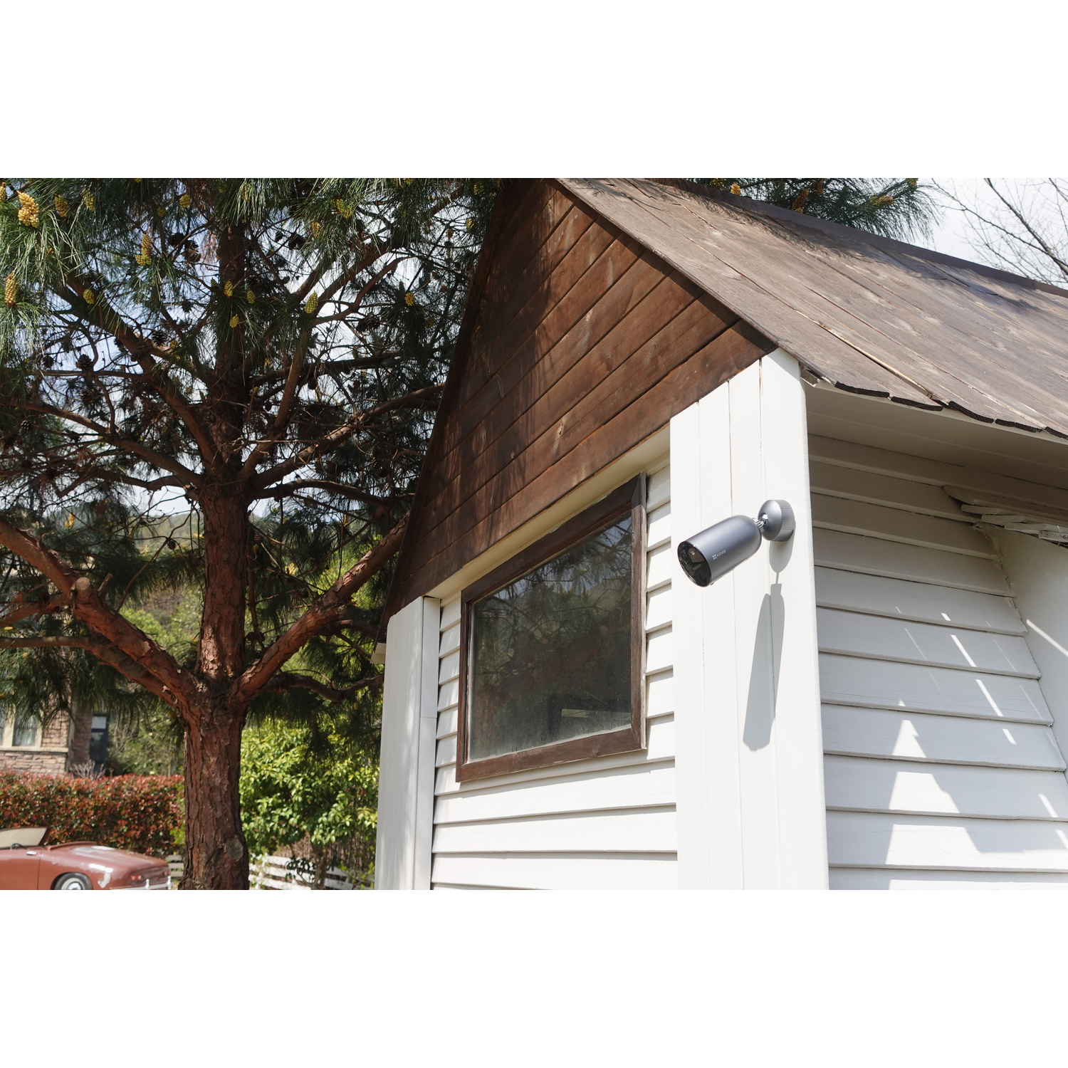 A black security camera on a white wall attached to a wooden shed.