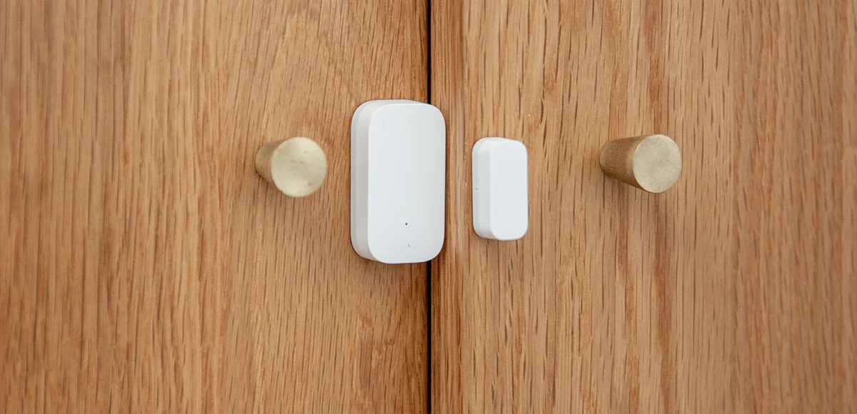 Białe czujniki inteligentnego domu przymocowane do drewnianych drzwi.