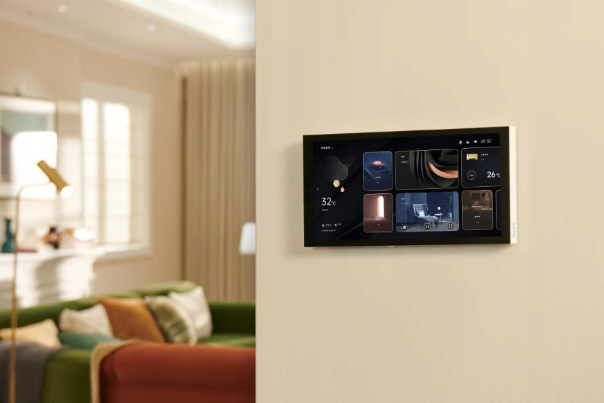 Panel sterowania inteligentnego domu na ścianie. Zielona sofa i lampa w tle.