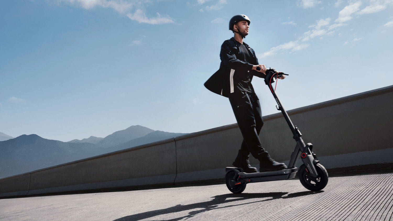 Un hombre en patinete con casco, montando en una carretera asfaltada.