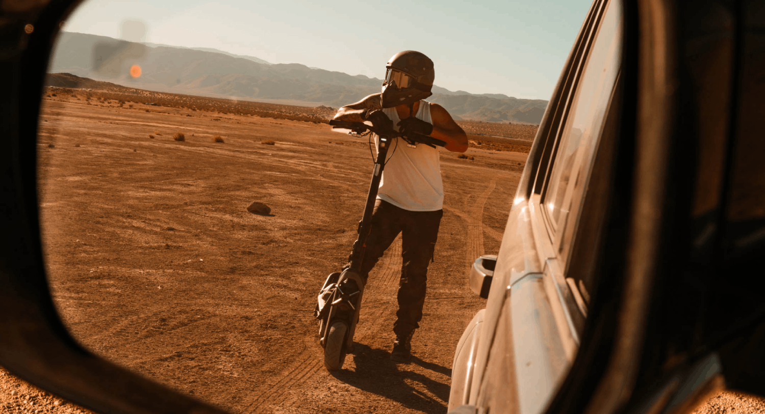 Hombre en un scooter en el desierto, reflejado en el espejo lateral de un coche.
