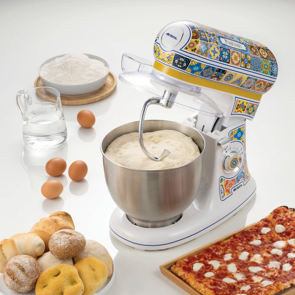 Fehér mixer tésztával a tálban, hozzávalók körülötte. Pizza és kenyér az oldalon.