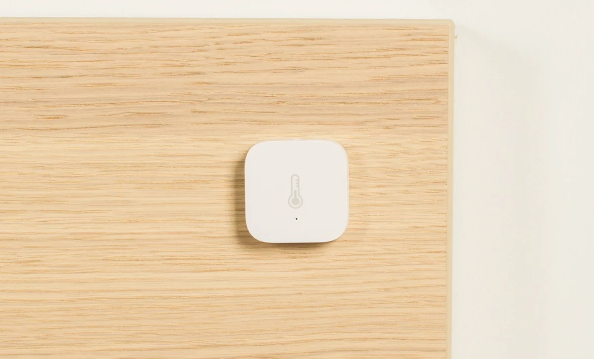 Biały kwadratowy czujnik temperatury smart home na drewnianej powierzchni, prosty design.