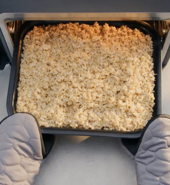 Brązowy ryż w blasze do pieczenia, trzymany przez rękawice kuchenne, gotowy do wyjęcia z piekarnika.