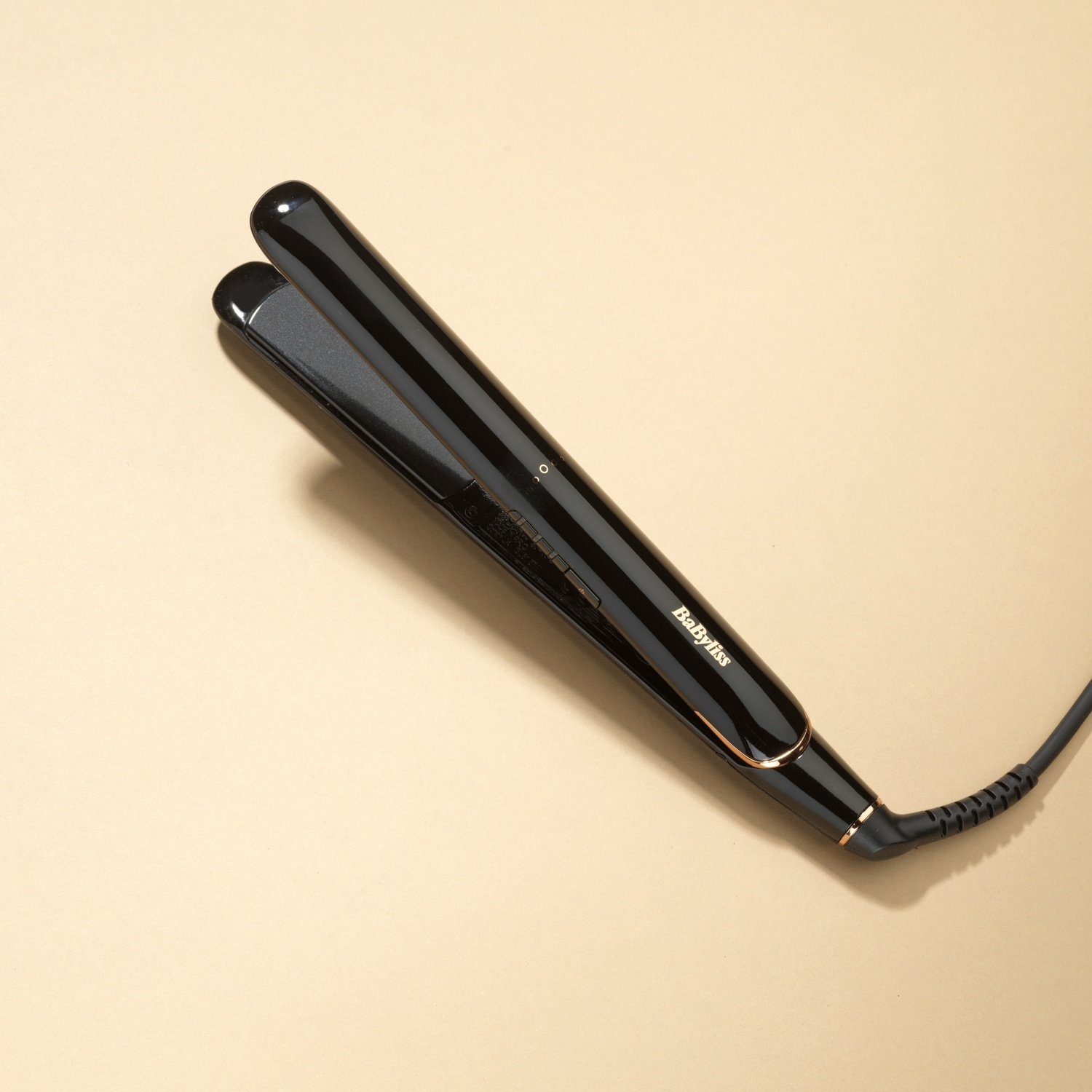 Piastra per capelli nera con dettagli oro rosa, su sfondo beige.
