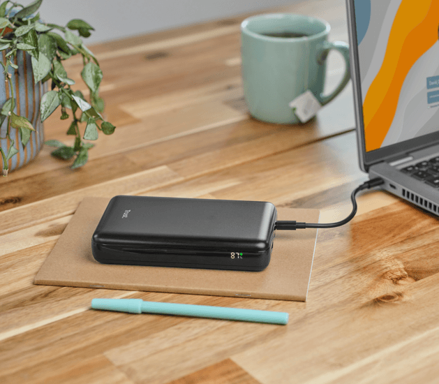 Laptop power bankkal és tollal egy faasztalon.