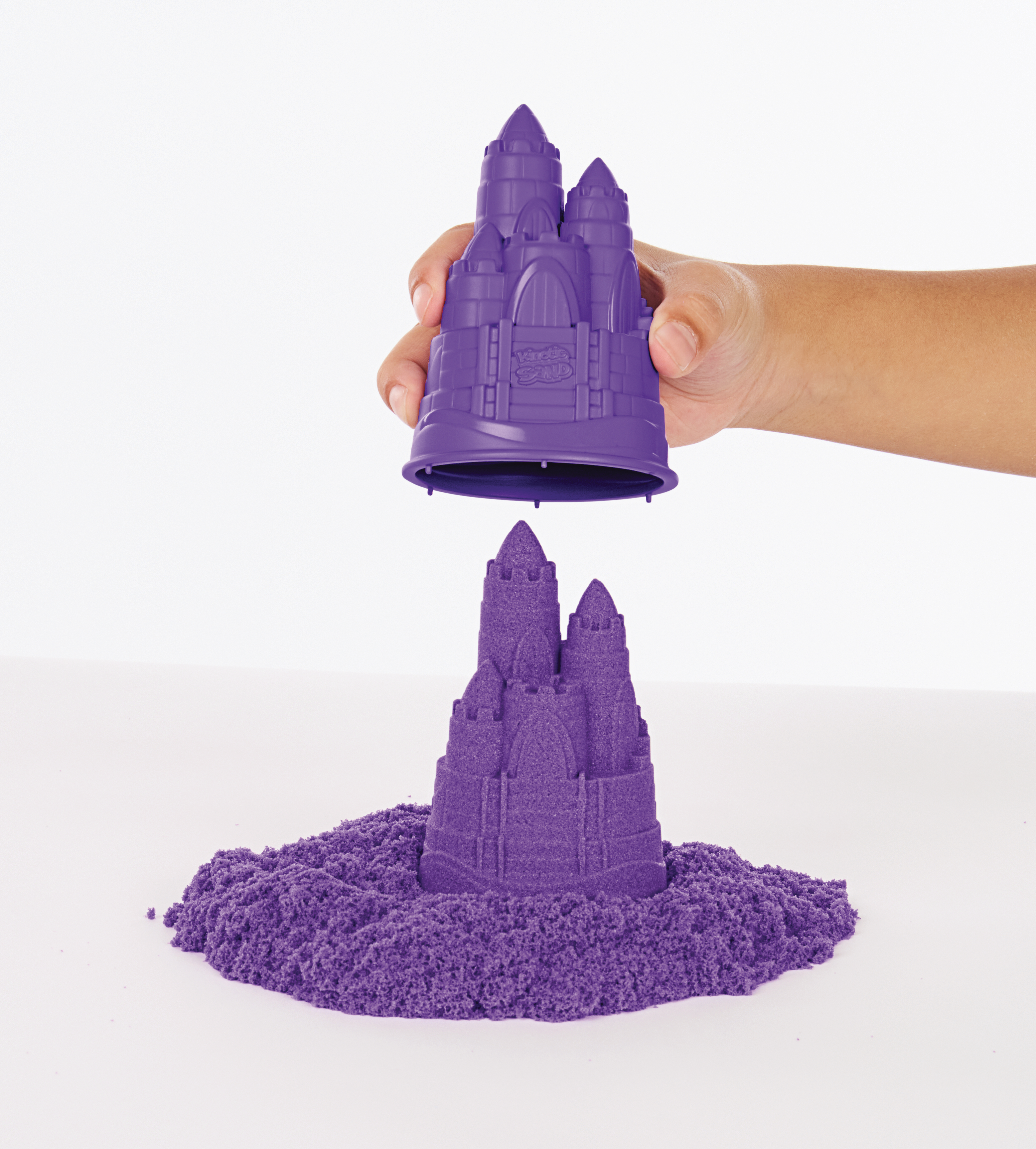 Eine Hand verwendet eine lila Burgform, um eine Sandburg zu erstellen. Der Sand ist lila.