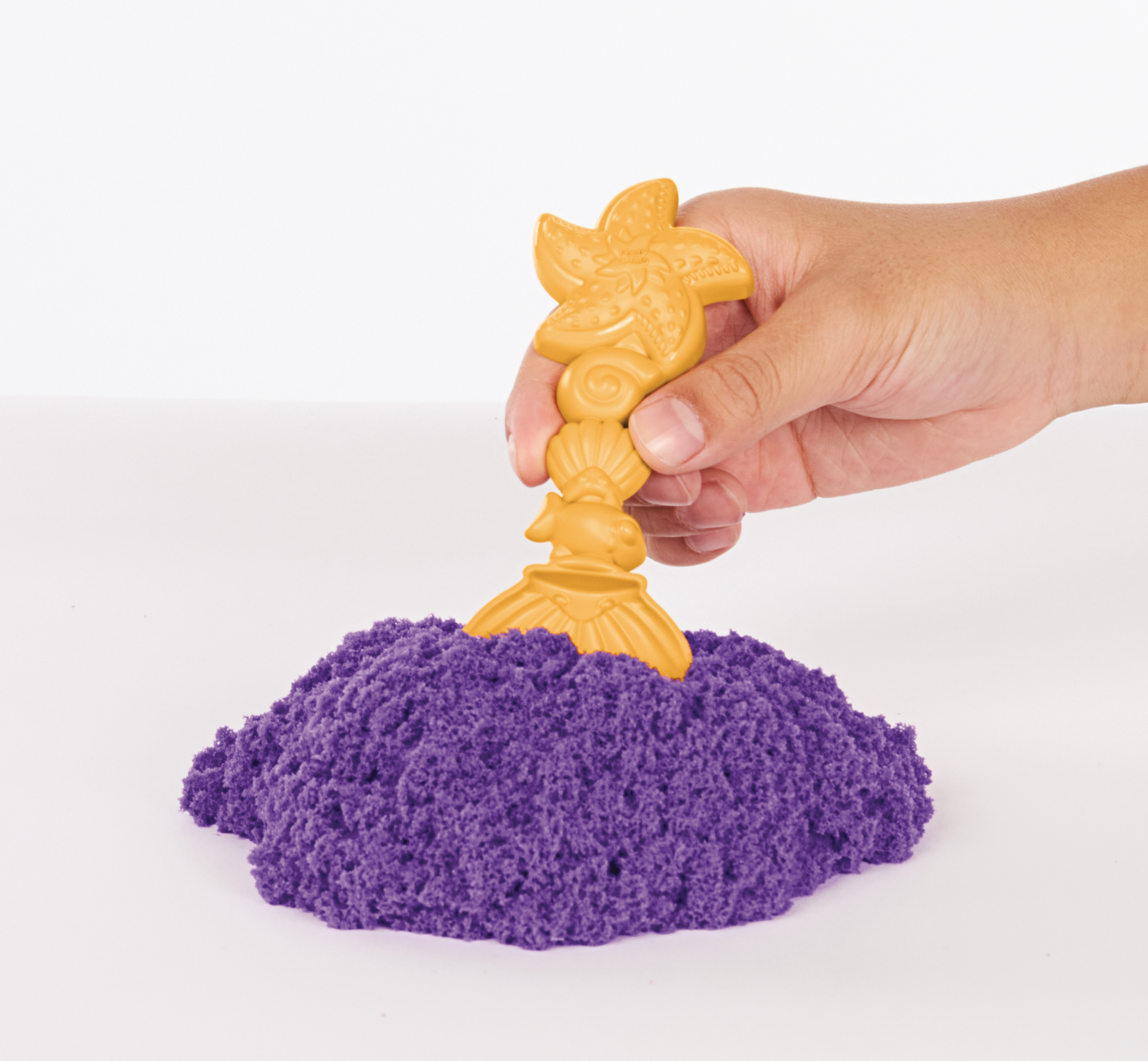 Hand hält eine Sandburgform über violettem Kinetiksand. Die Form hat ein Seestern-Design.
