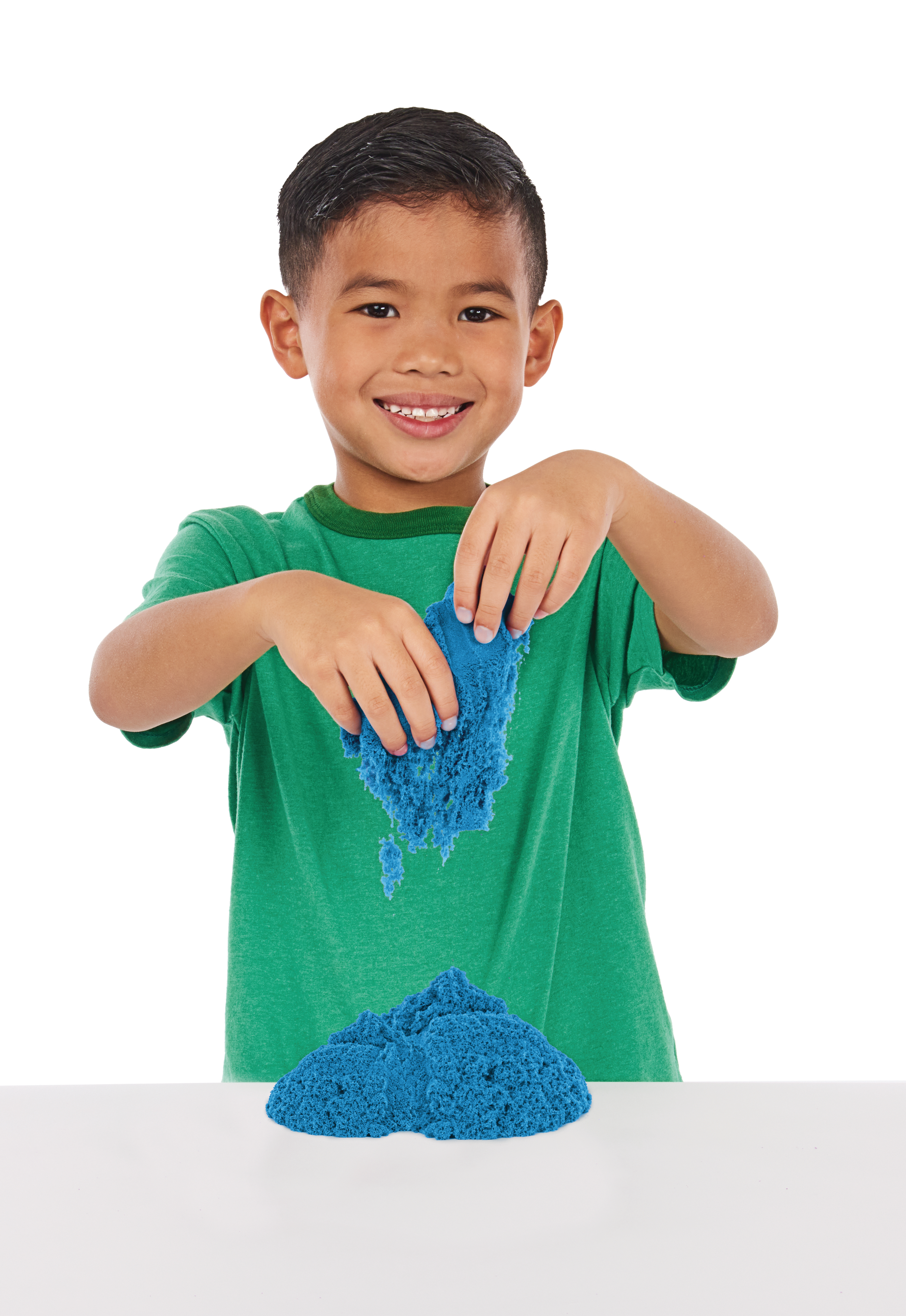 Junge spielt mit blauem kinetischen Sand auf weißer Oberfläche. Er lächelt.