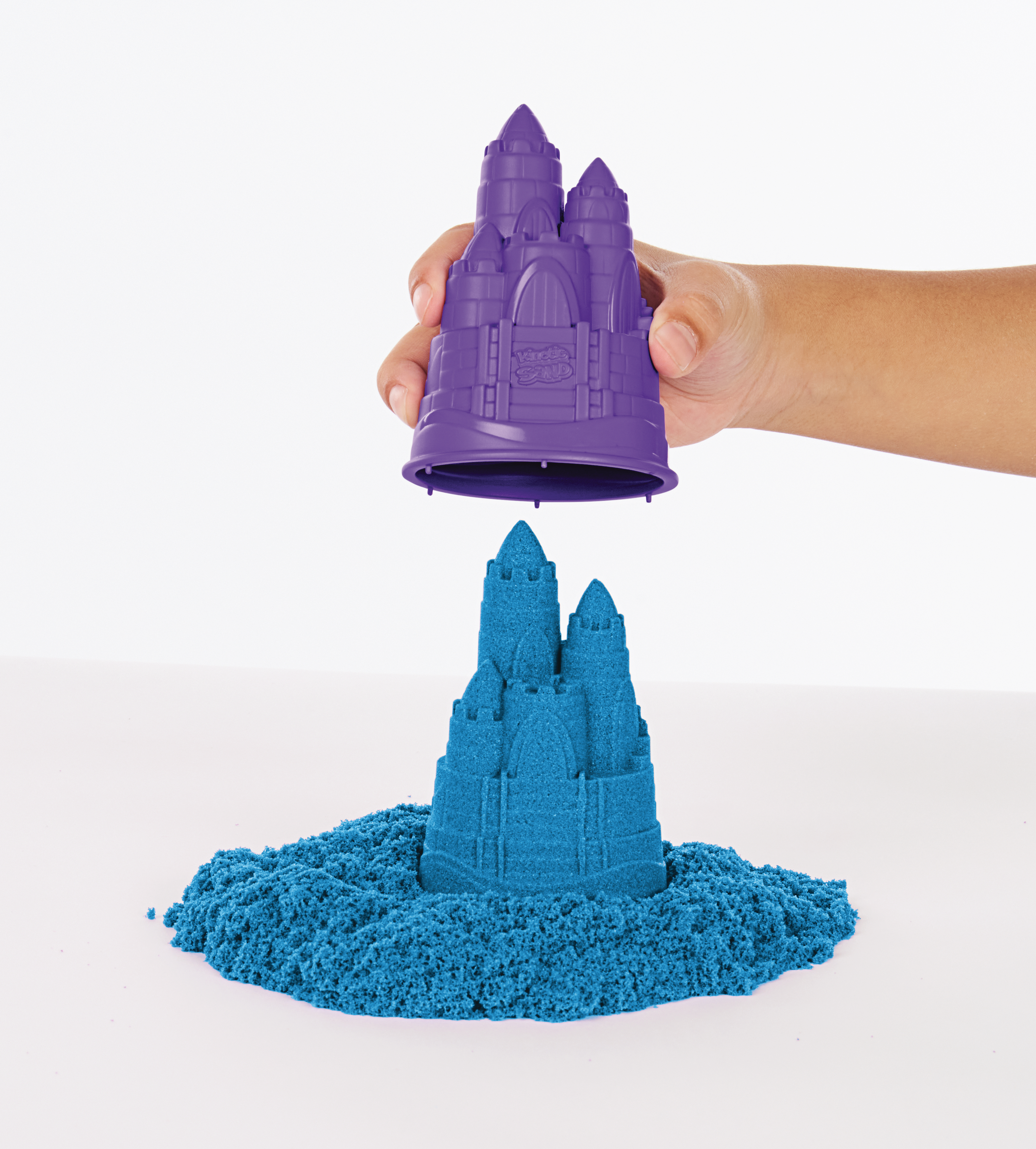 Eine Hand, die eine lila Burgform über eine blaue Sandburg legt.