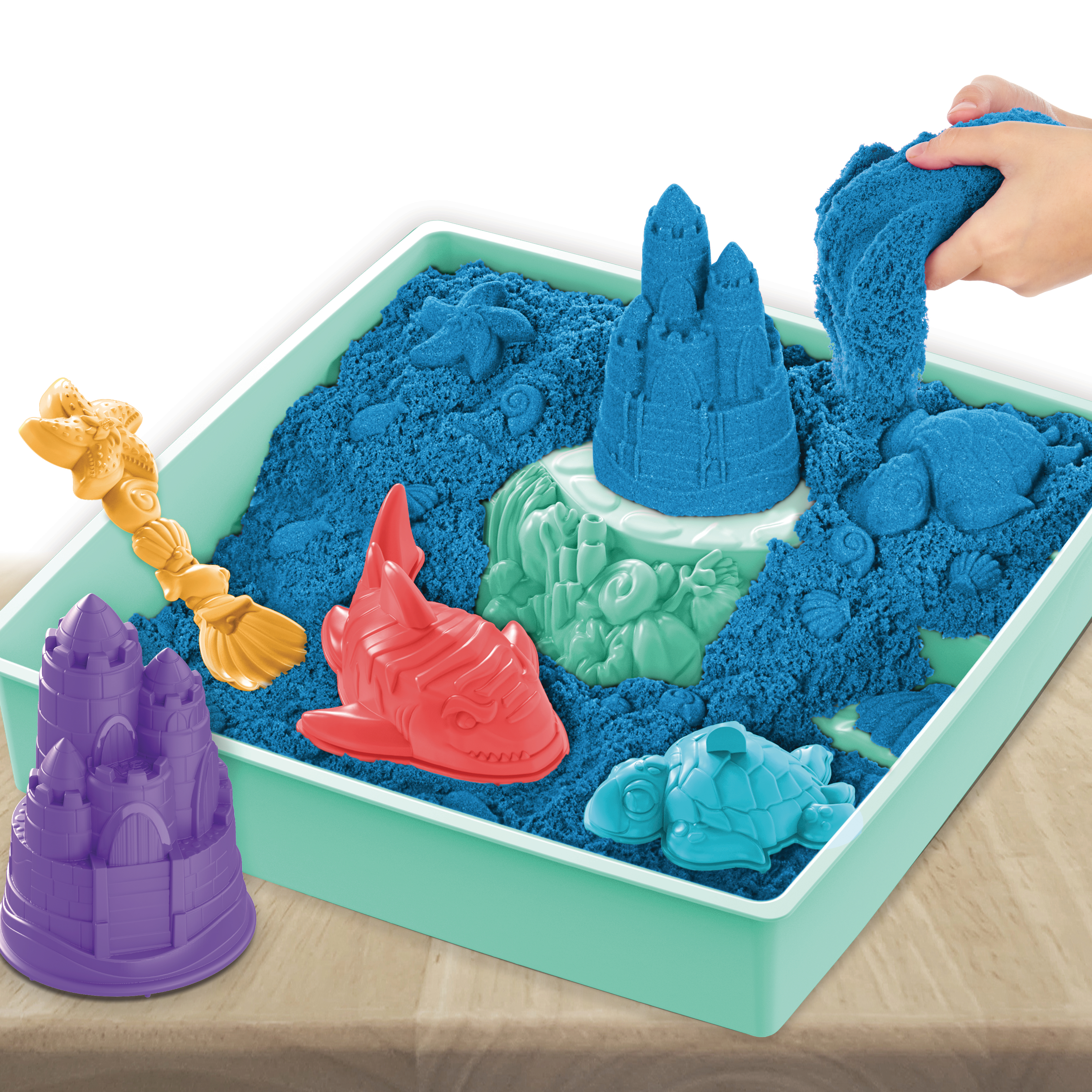 Sandkunst-Set. Blauer Sand in einer Schale. Bunte Sandformen und eine Hand, die den Sand formt.