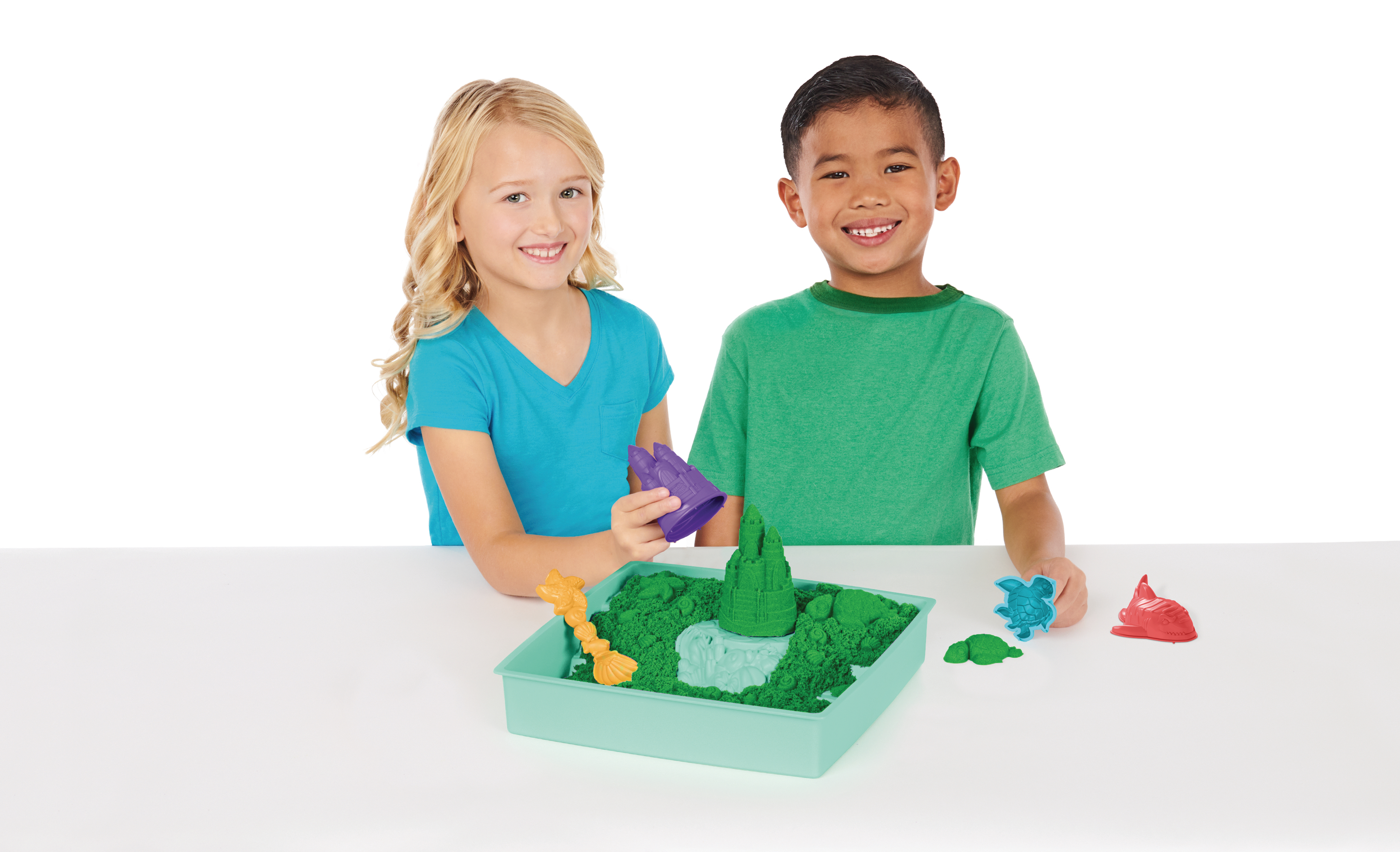 Zwei Kinder lächeln, während sie mit Kinetiksand und Formen spielen, eine grüne Schale und weißer Hintergrund.
