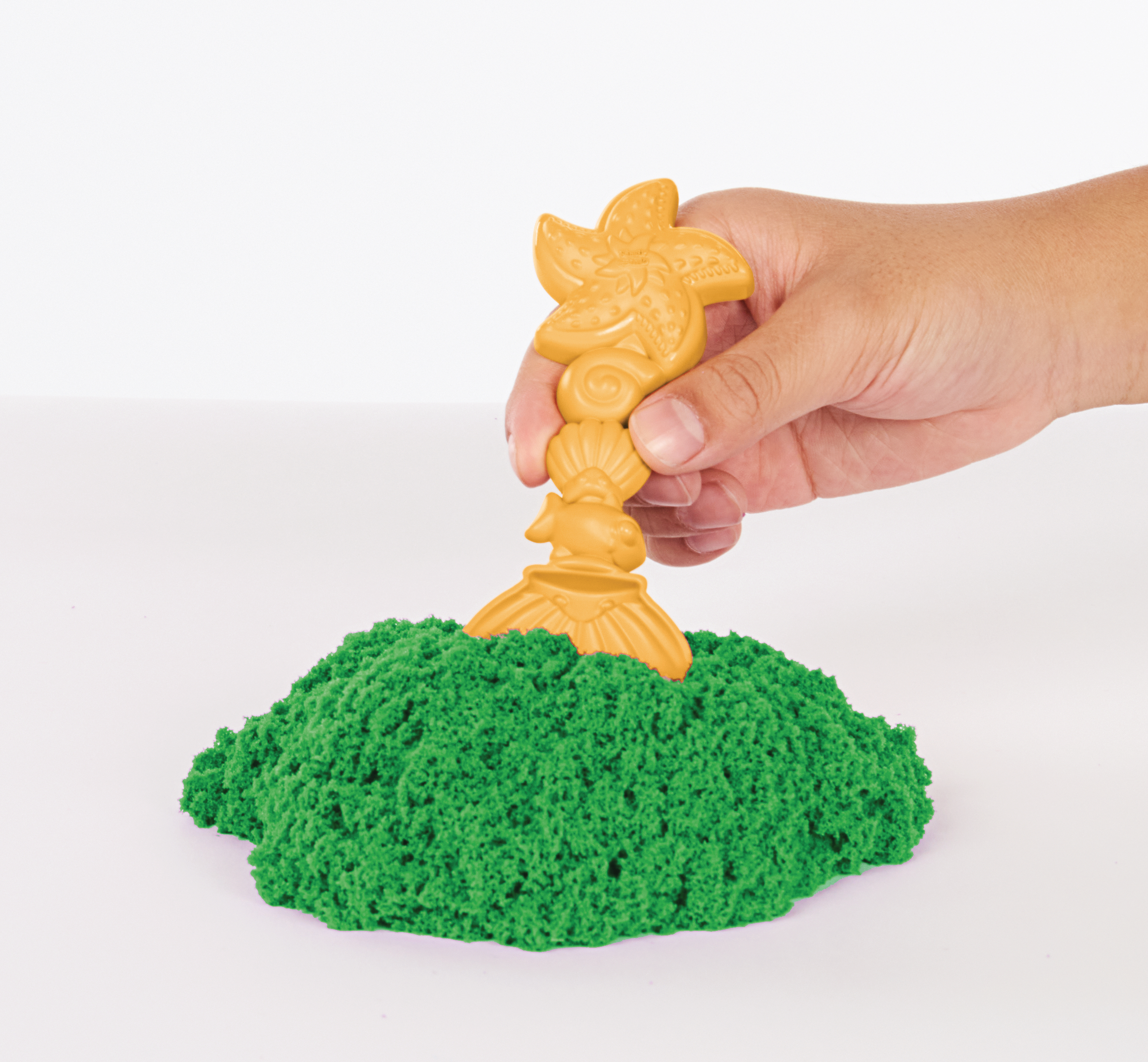 Hand pflanzt gelbe Palme in grünem Kinetiksand. Weißer Hintergrund. Sand sieht aus wie Gras.