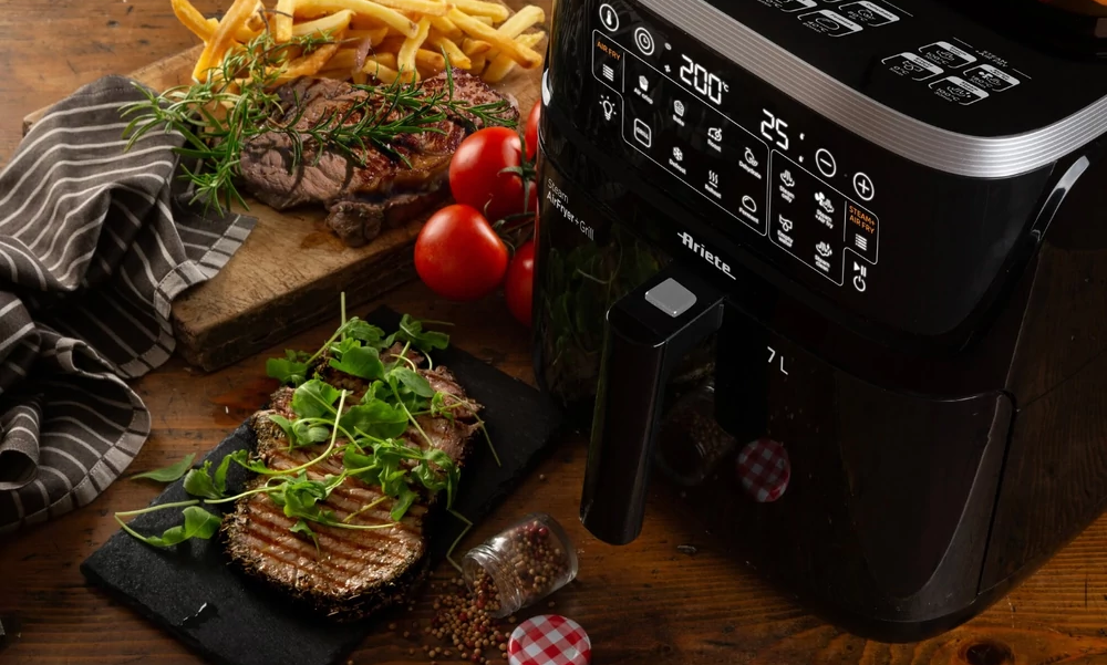 Fekete légsütő sült steakkel, paradicsommal és fűszernövényekkel egy faasztalon.