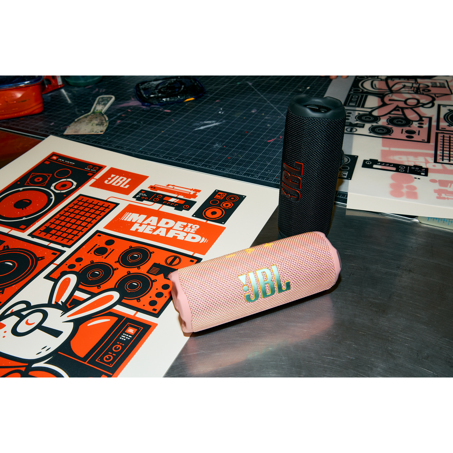 Two JBL speakers, pink and black, and a poster with JBL logo and design.