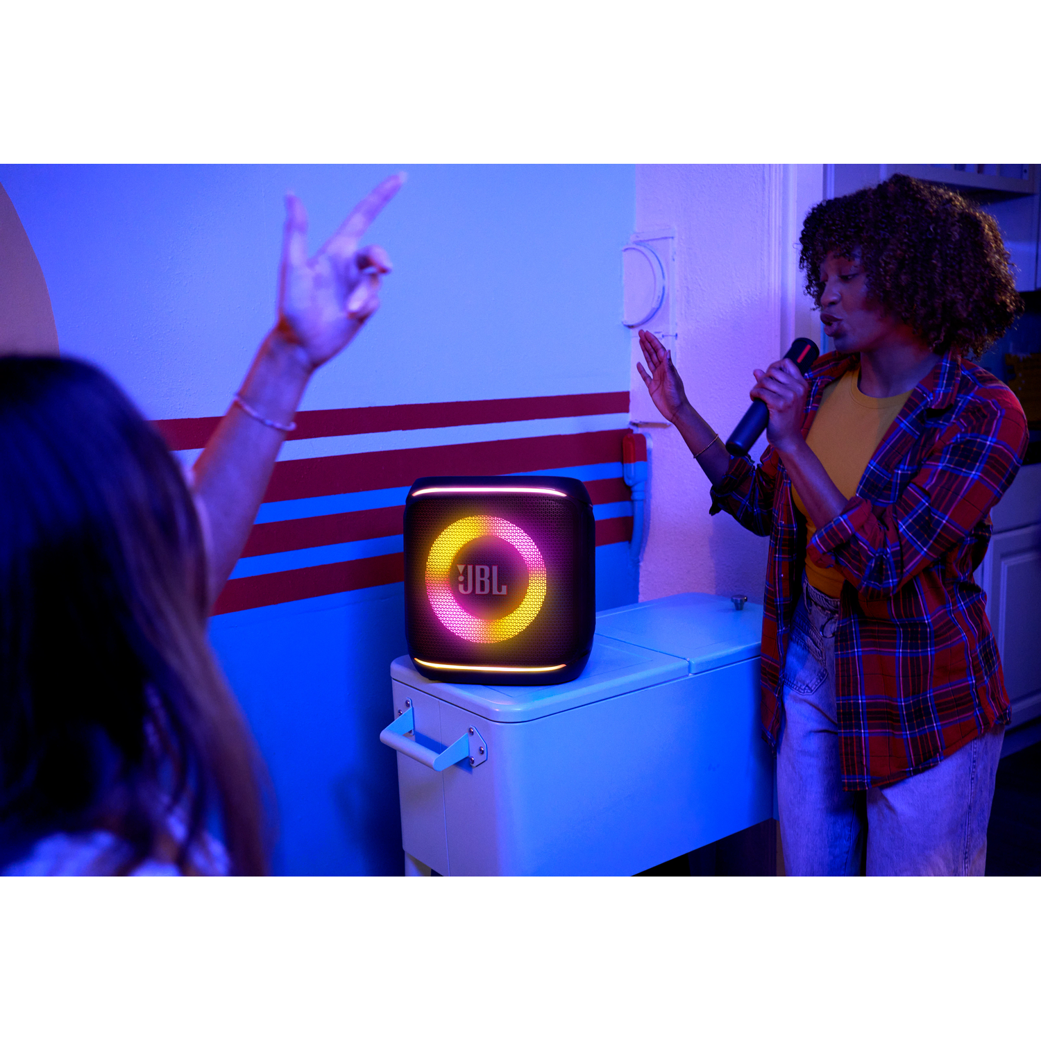 Vrouw zingt met microfoon. JBL-luidspreker met gekleurde lichten op een koeler.