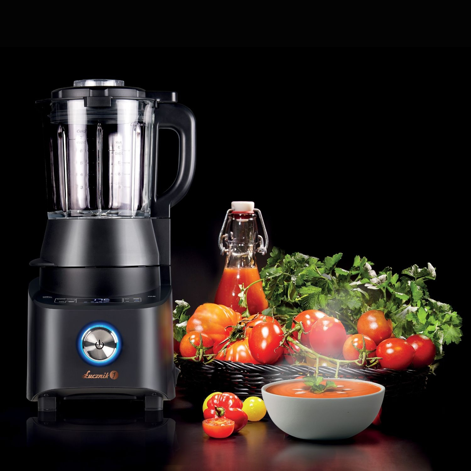 Czarny blender z pomidorami, pietruszką, sokiem pomidorowym i miską zupy na czarnej powierzchni.