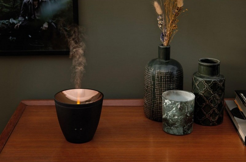 Czarny dyfuzor z parą, na drewnianym stole. W tle wazony i obraz w ramie.