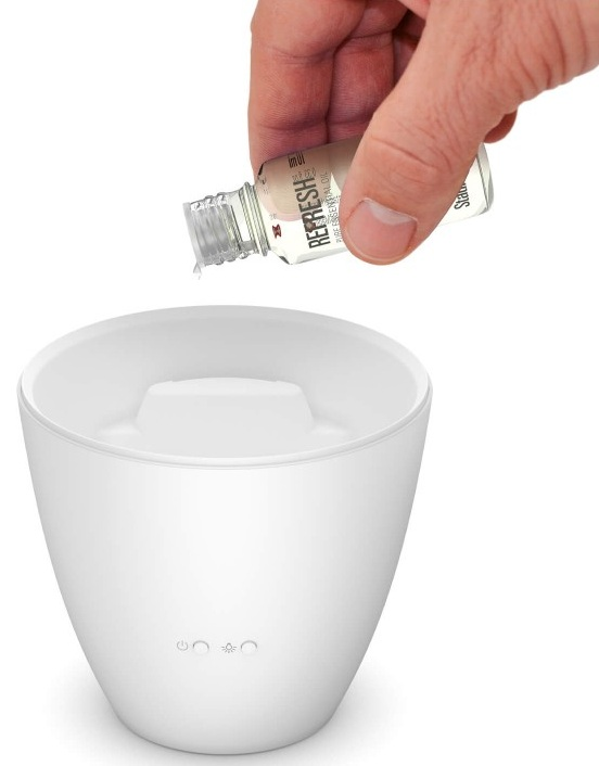 Ręka wlewa płyn z małej butelki do białego, stożkowatego dyfuzora do aromaterapii.