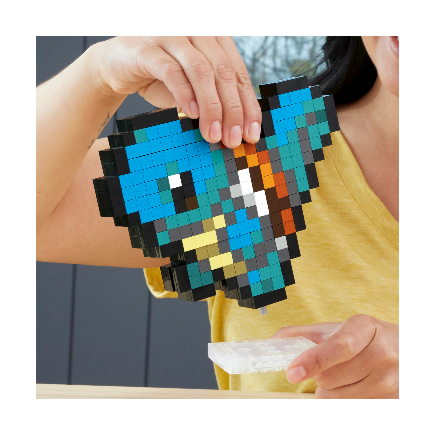 Una persona che tiene un'opera d'arte a forma di cuore pixelata con colori blu e marrone.