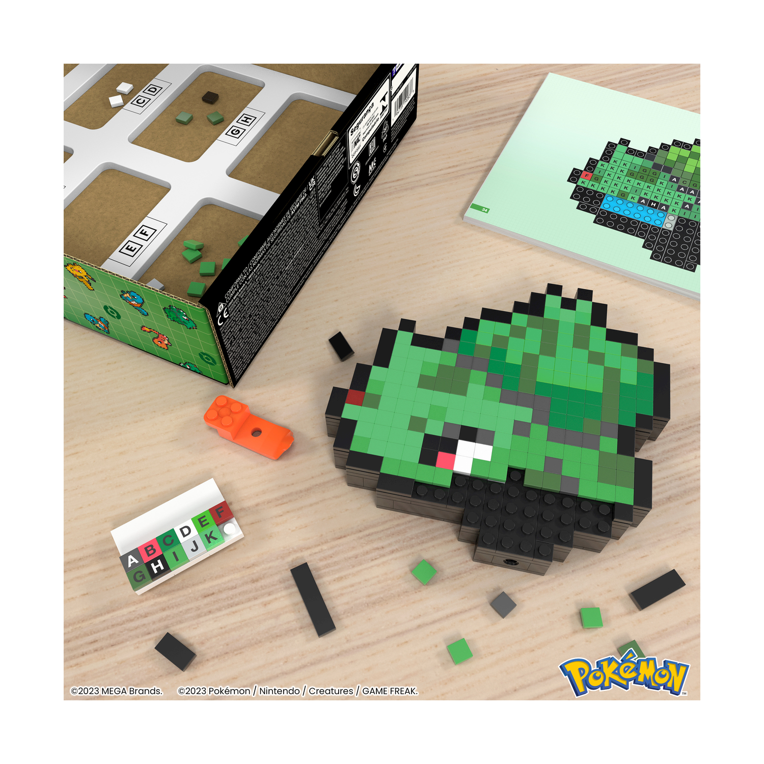 Un modello pixelato di Bulbasaur fatto di blocchi è accanto a una scatola di gioco e istruzioni. Altri blocchi sono presenti.