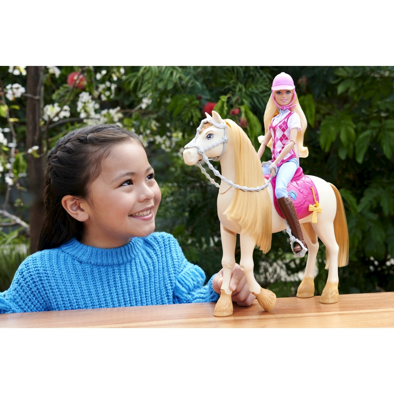 Una bambina guarda una bambola Barbie che cavalca un cavallo bianco. La bambola indossa casco e gilet.