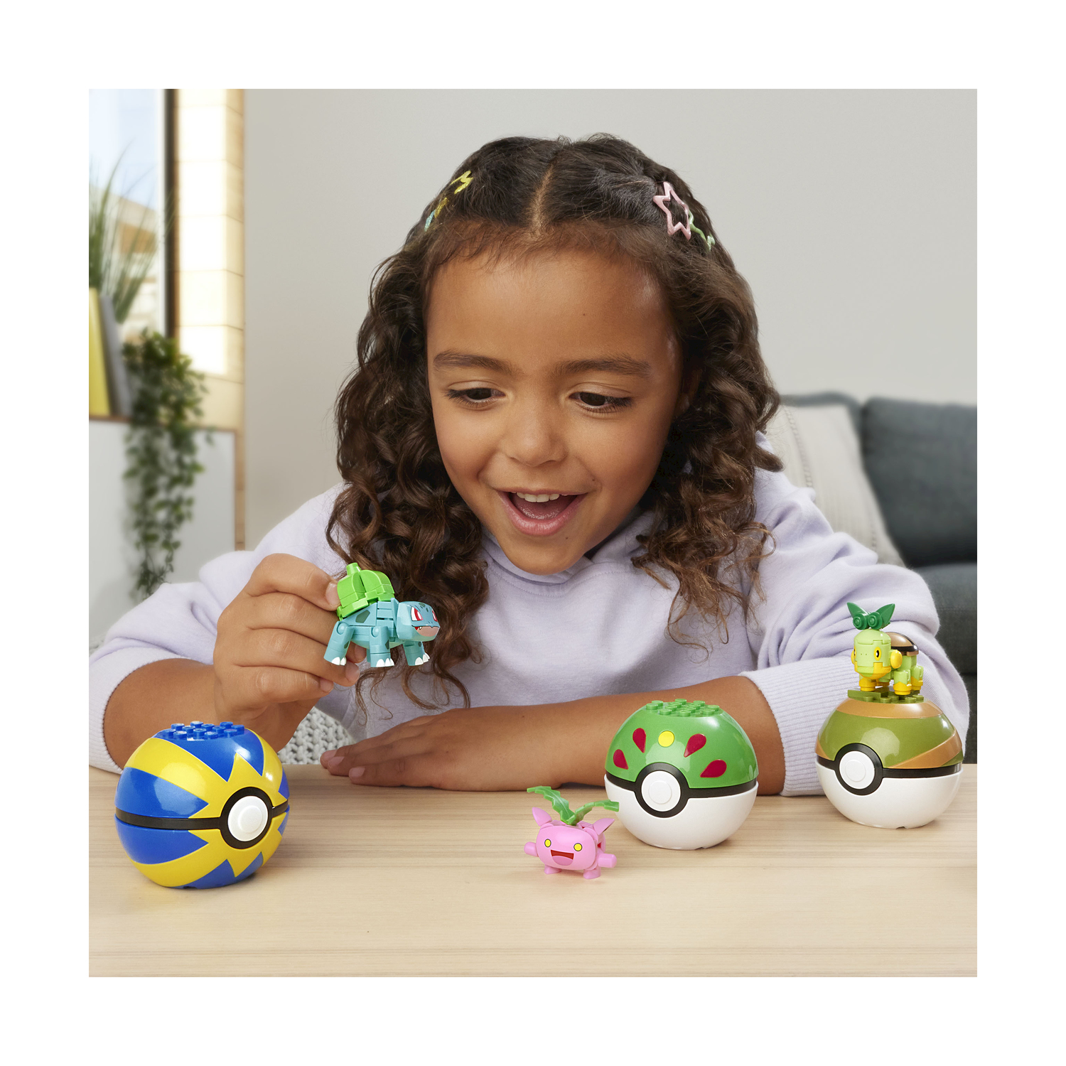 Una bambina che tiene una figura di Bulbasaur e un bambino che tiene una figura di Squirtle con giocattoli Pokémon su un tavolo.