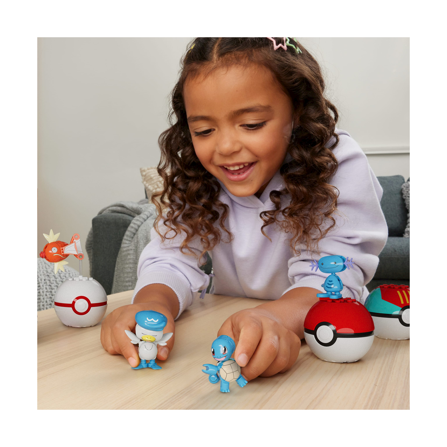 Ragazza con giocattoli. Giocattoli Pokémon su un tavolo. Tre pokéball e tre personaggi.