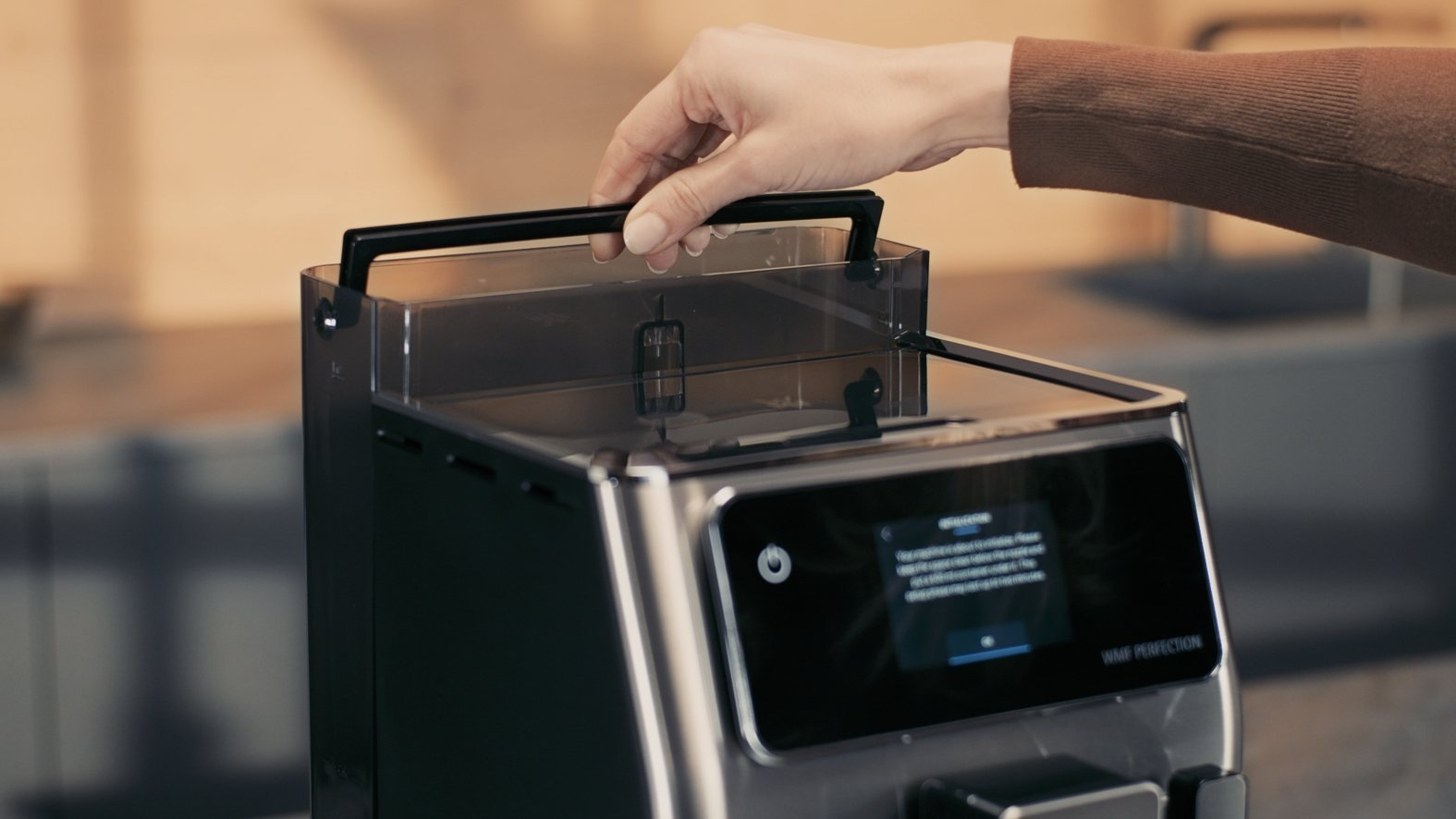 Ręka osoby otwierająca zbiornik wody w ekspresie do kawy.