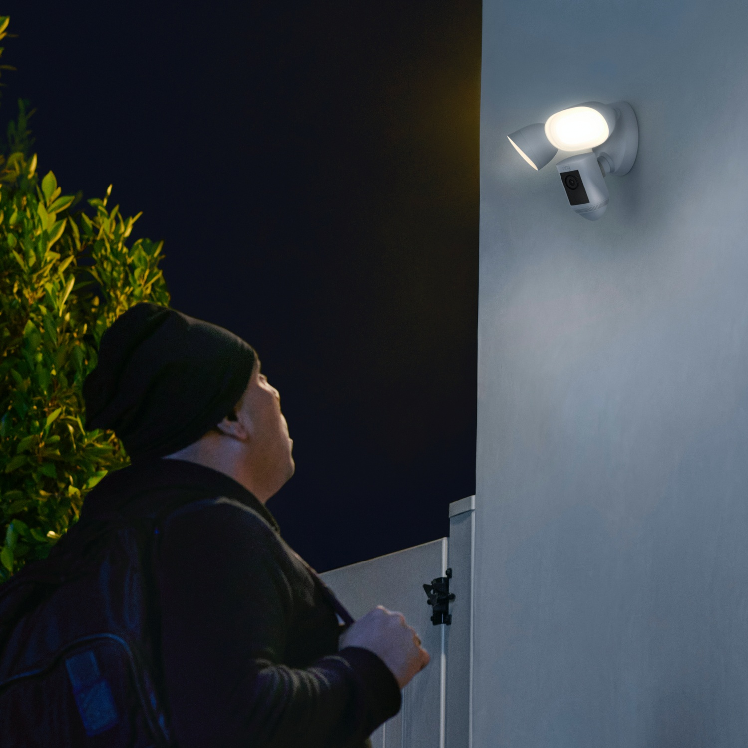 Een persoon kijkt 's nachts naar een veiligheidslamp aan een huismuur.