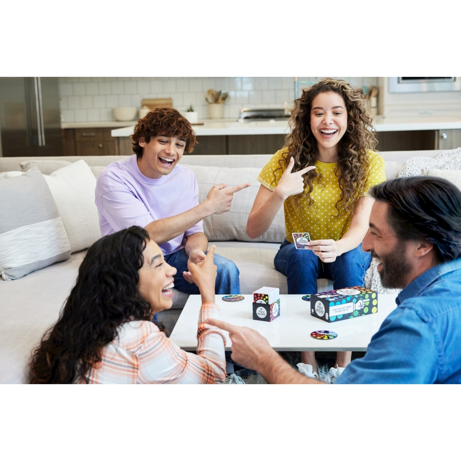 Quattro persone ridono e indicano, giocando con carte e un contenitore per il gioco.