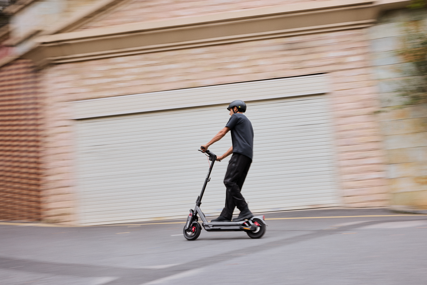 Persona montando un scooter en una carretera asfaltada, fondo borroso con un edificio.