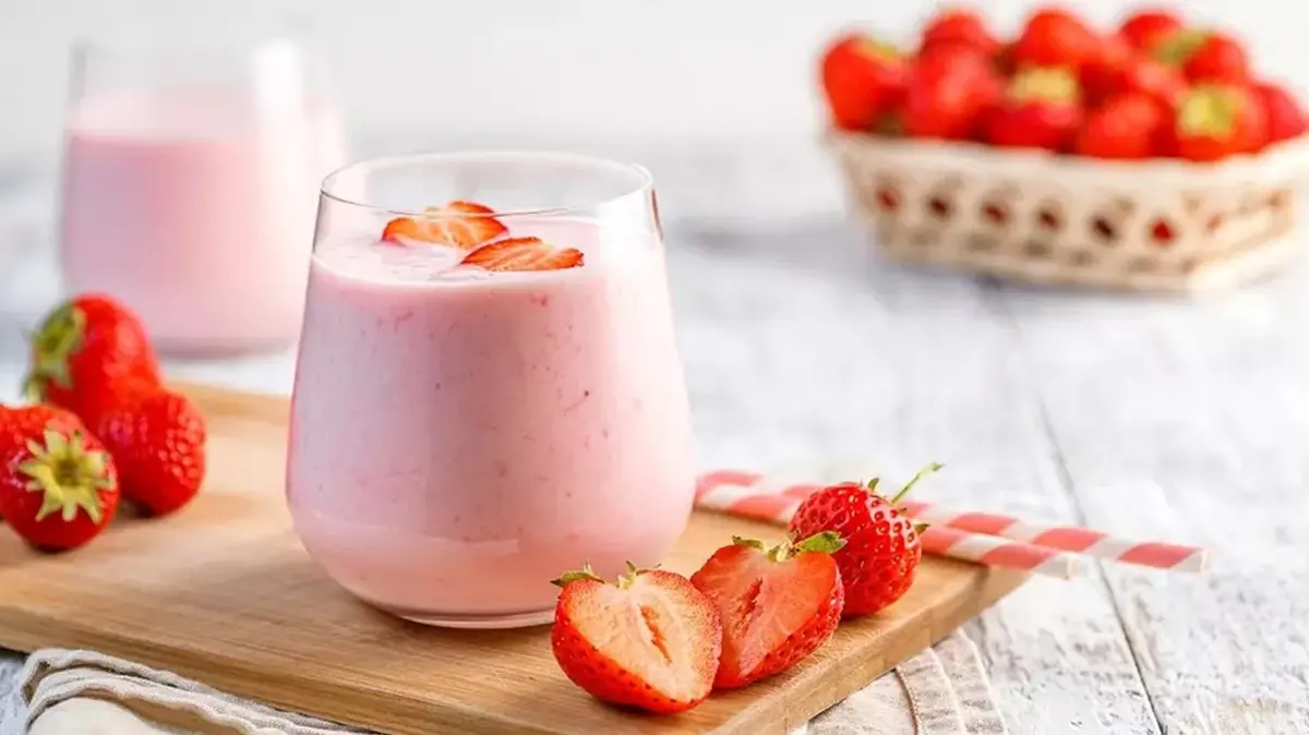 Pembe içecek ve çilek dilimleri olan bardak. Arka planda çilekler ve sepet. Ahşap tahta.