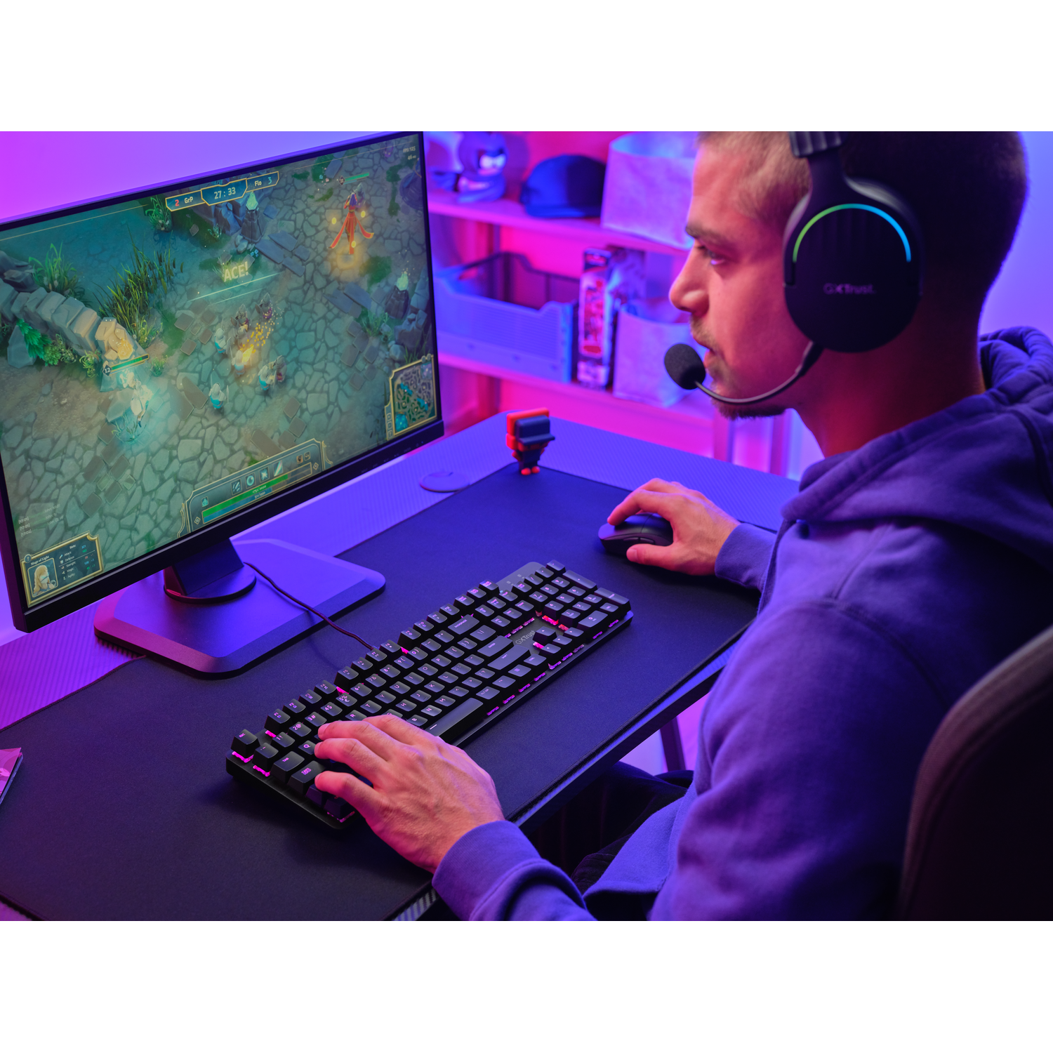 Een man is aan het gamen met een toetsenbord, muis en headset. De monitor toont een spel met een kleurrijke omgeving.