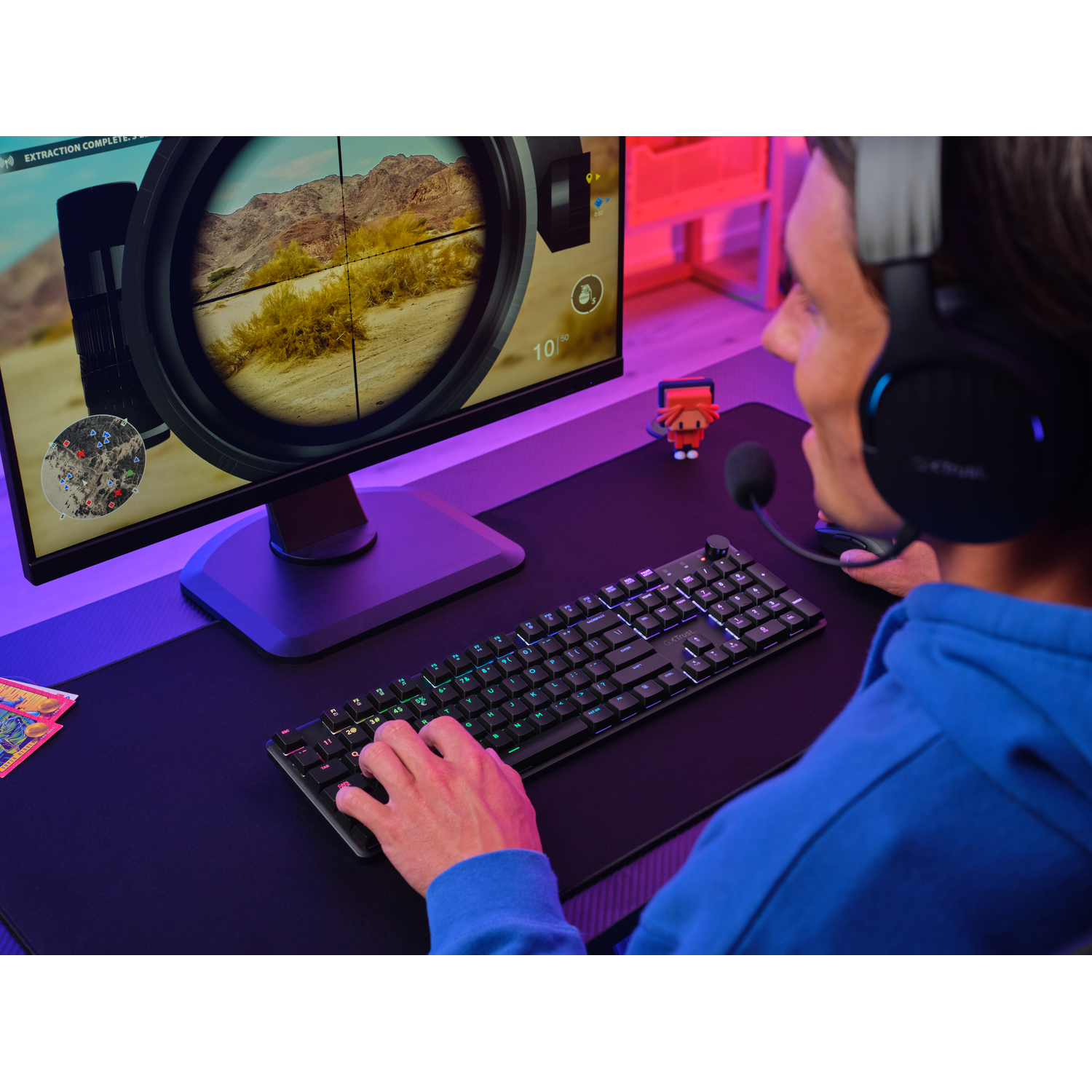 A person is gaming on a computer. There is a keyboard, monitor, and headset visible.
