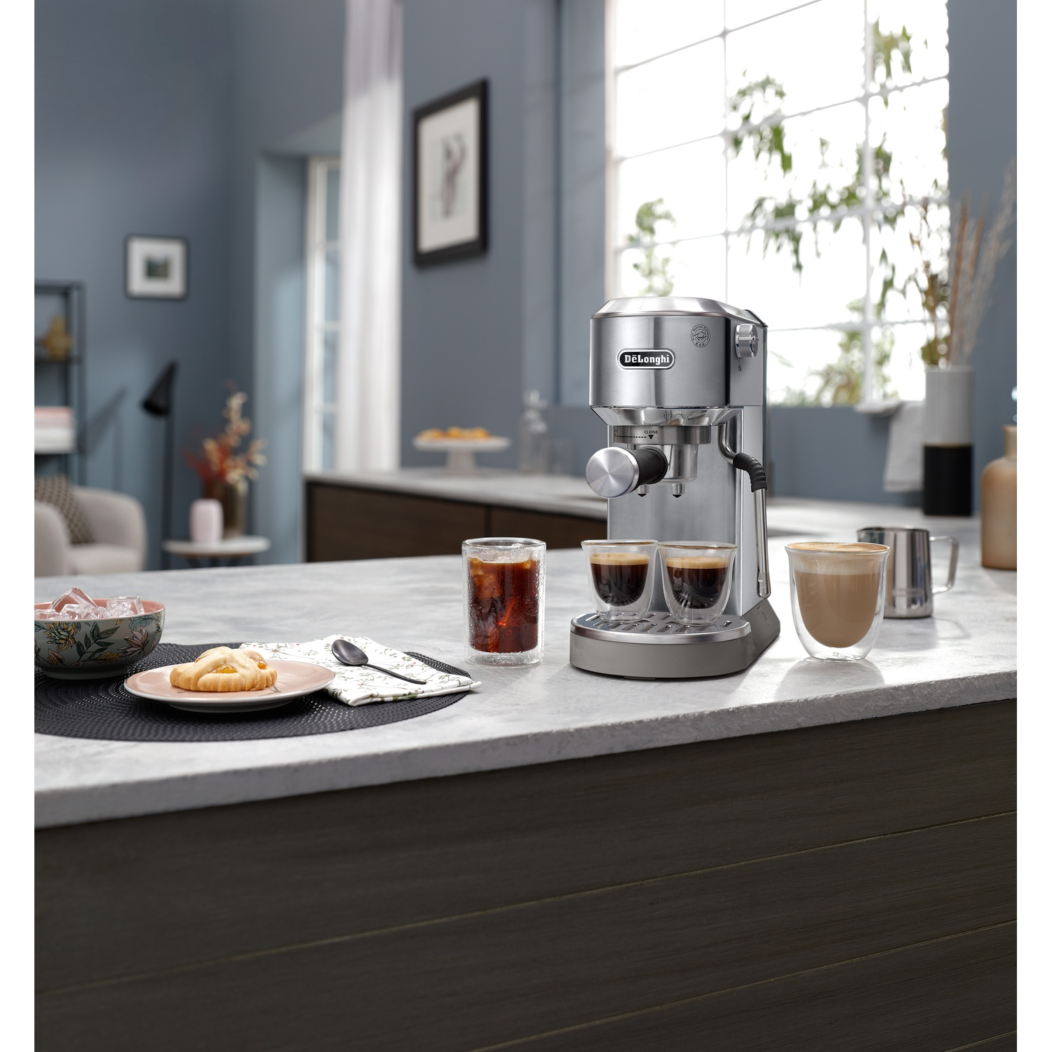 Coffee machine with two espresso shots in glasses, another glass of iced coffee, and a pastry.