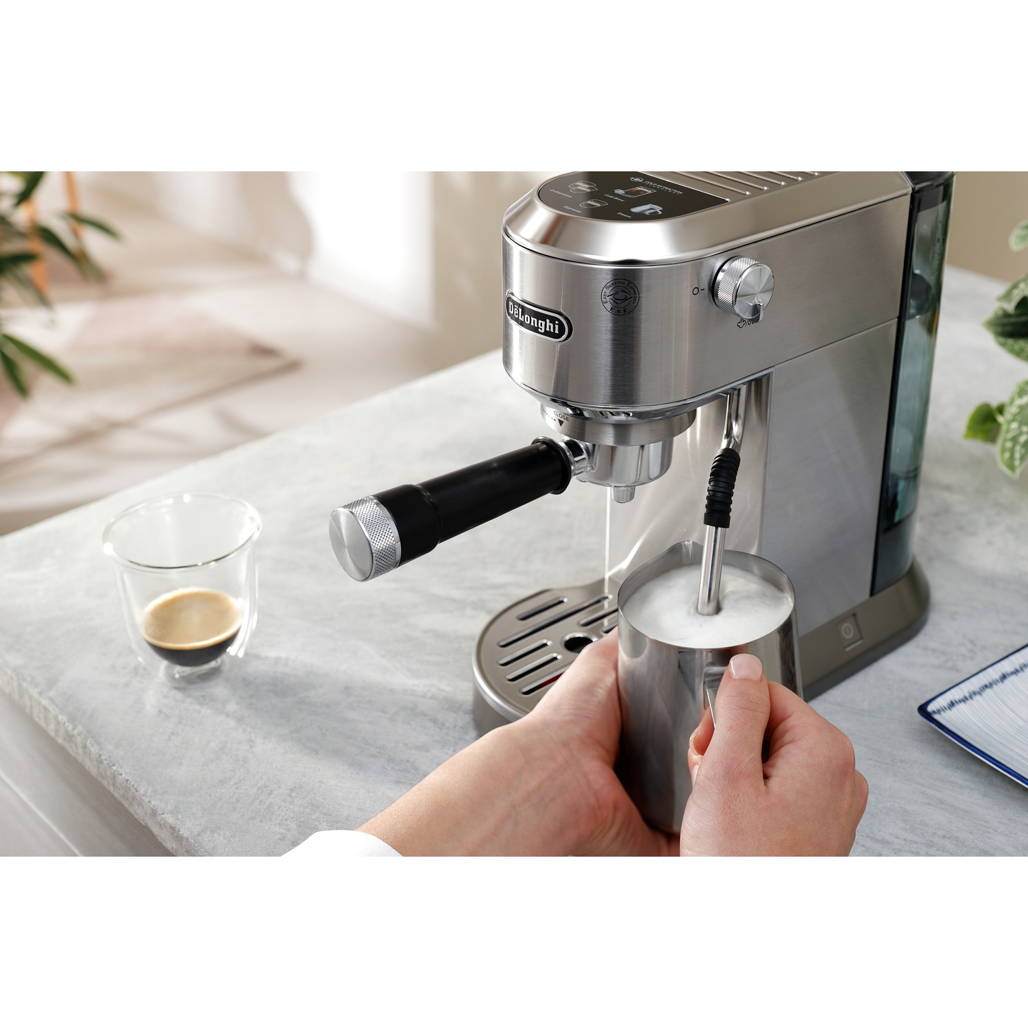 A person pouring milk into a cup of coffee using an espresso machine.