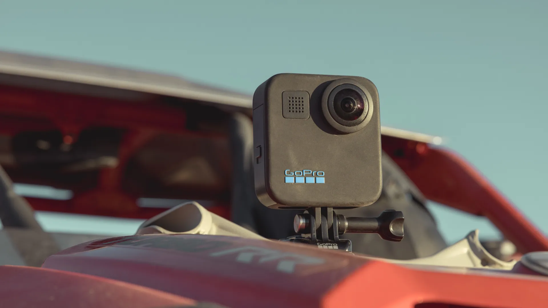 Una fotocamera GoPro nera è montata su un veicolo rosso, contro un cielo azzurro chiaro.