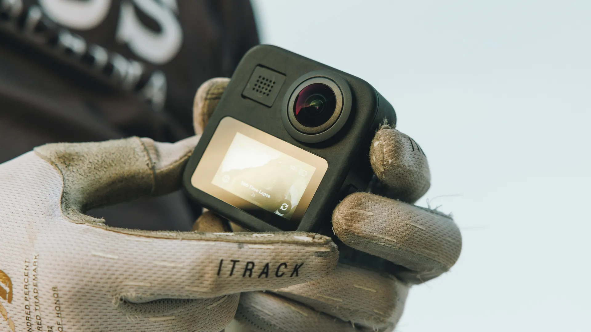 Fotocamera GoPro tenuta in mani guantate. Mostra lo schermo con un video in riproduzione.