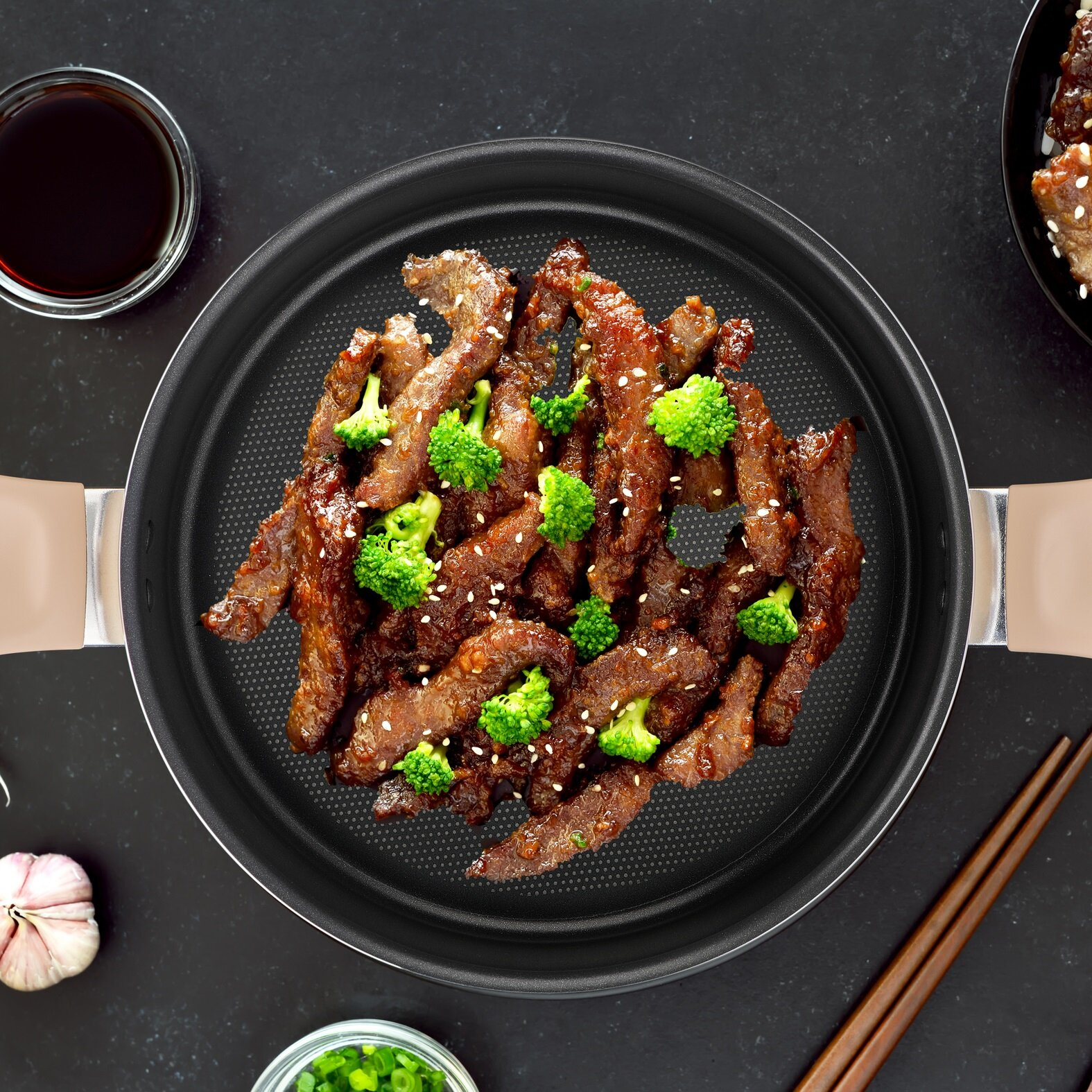 Patelnia z gotowaną wołowiną i brokułami z nasionami sezamu na ciemnej powierzchni. Obecne pałeczki i miski.