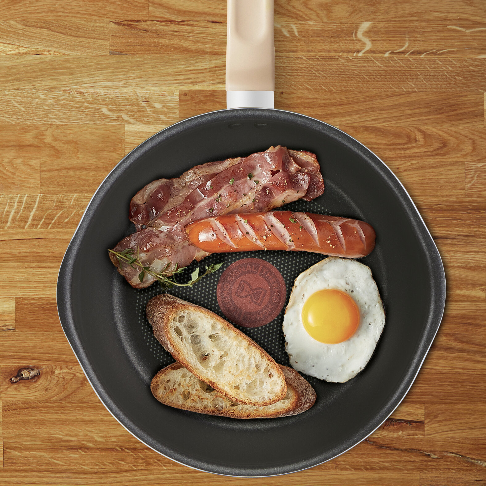 Patelnia z boczkiem, kiełbasą, jajkiem sadzonym i kromkami chleba na drewnianej powierzchni.