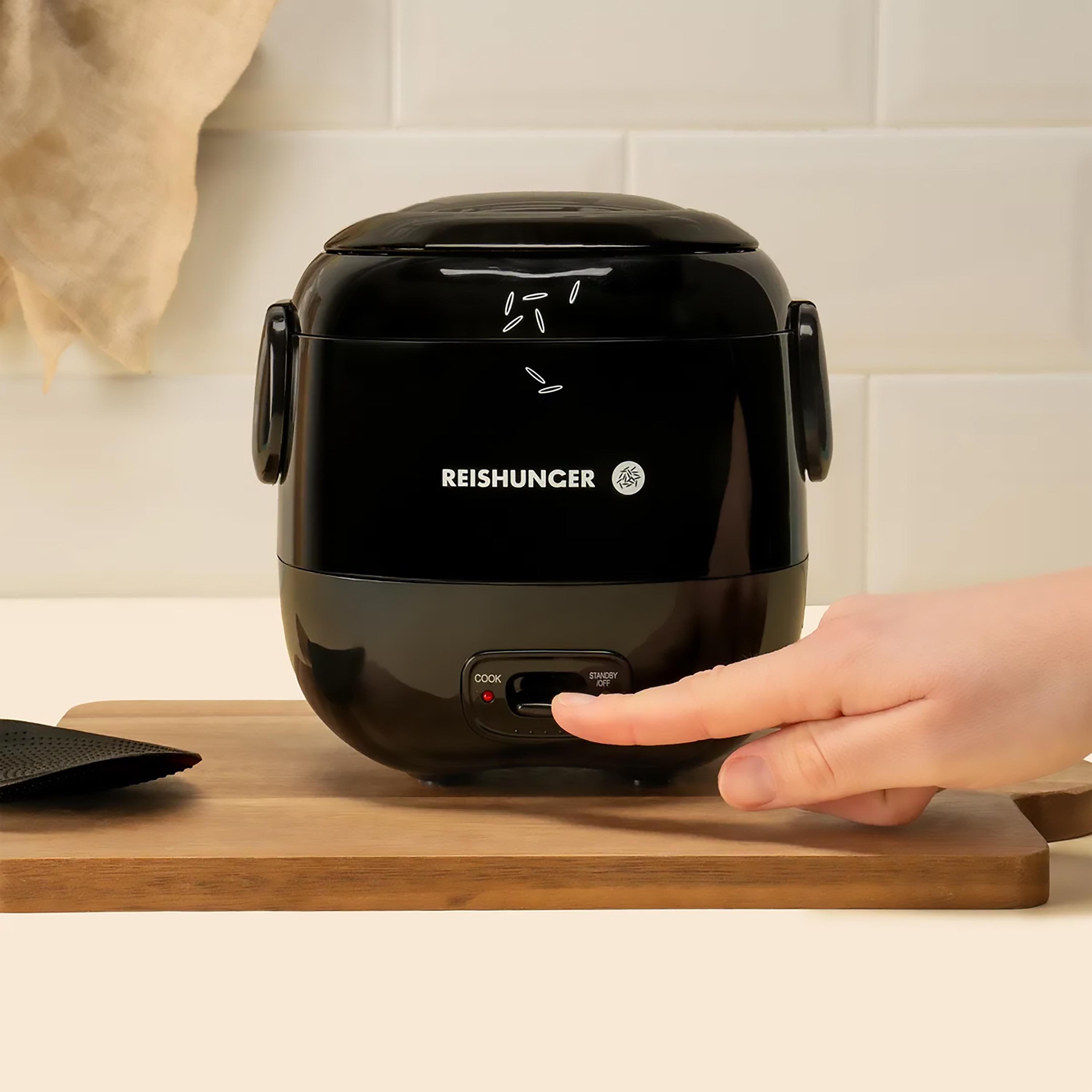 Schwarzer Reiskocher mit einem Finger, der die 'Cook'-Taste drückt.