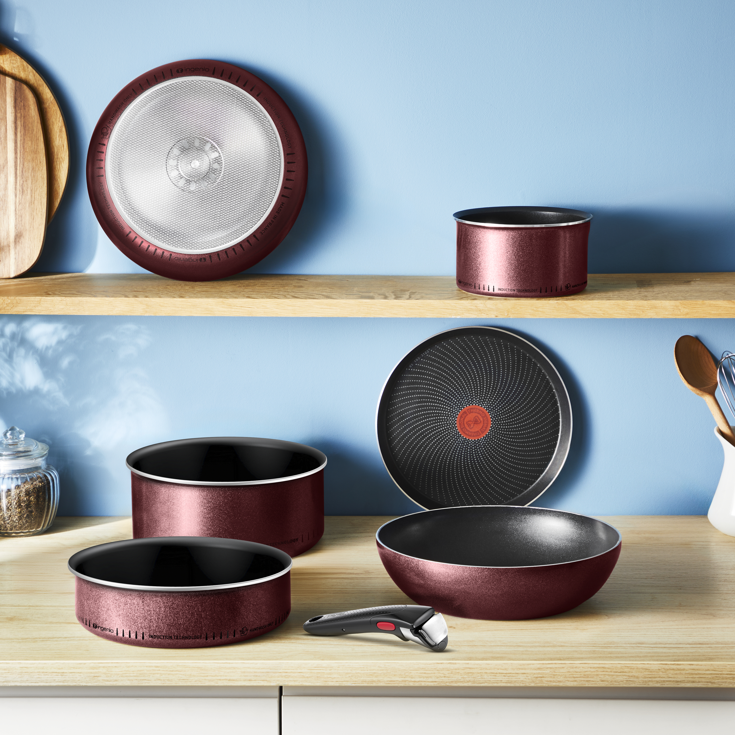 Zestaw czerwonych patelni i pokrywek na drewnianych półkach na tle niebieskiej ściany.