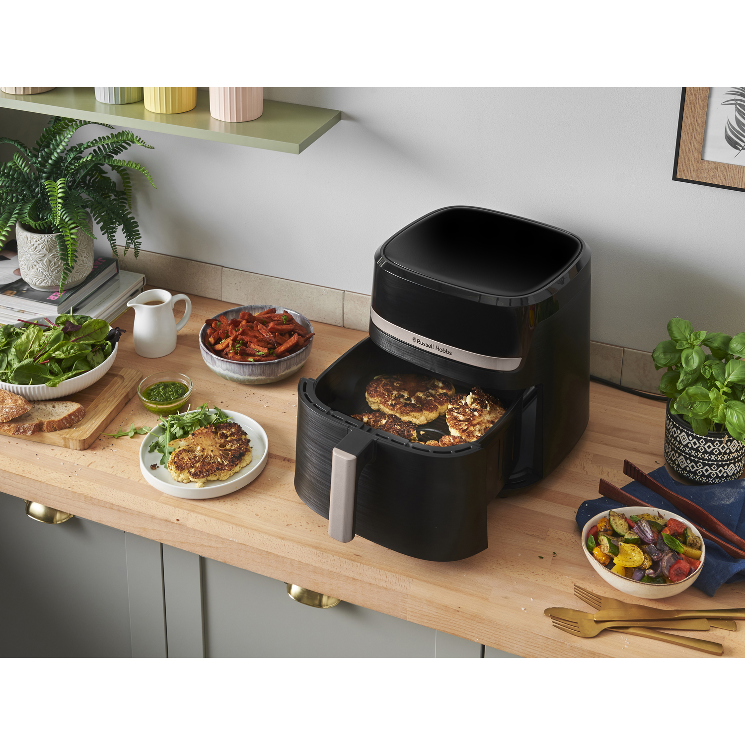 Airfryer met eten erin, andere etenswaren op het aanrecht en planten.