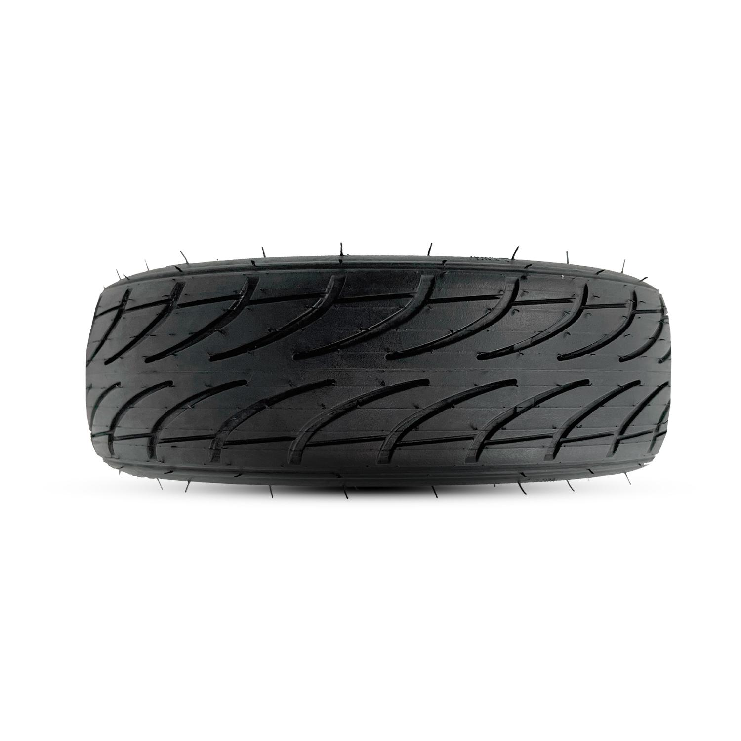 Un neumático de scooter negro con ranuras sobre fondo blanco, fotografiado desde un ángulo cercano.