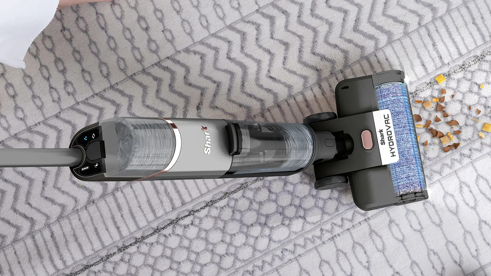 Szary i czarny odkurzacz Shark HydroVac na wzorzystym dywanie, czyszczący zanieczyszczenia.